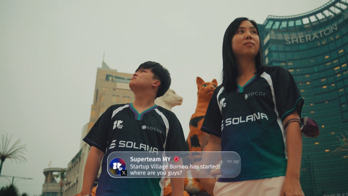 Two people wearing dark "SOLANA" and "SOCOE" branded jerseys stand looking upward in front of the Sheraton hotel, with a social media overlay from "Superteam MY" announcing "Startup Village Borneo has started! where are you guys?" The image captures the startup event atmosphere referenced in the post about their Amazing Race Day and first Connect event in Kuching with @RedotsClub, powered by Solana and SOCOE.