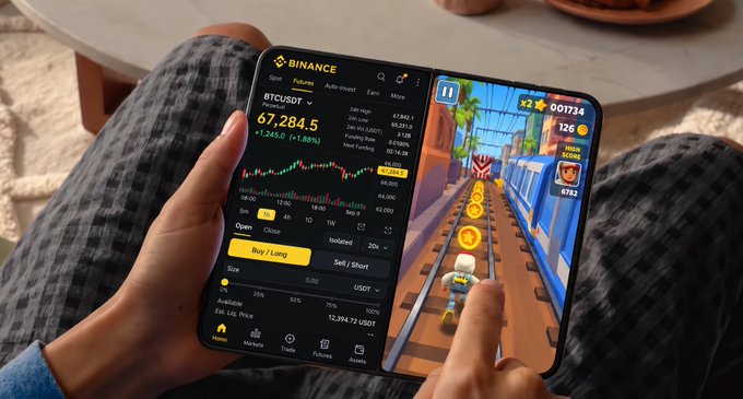 A person holds a device with a foldable dual-screen setup, displaying Binance's BTC/USDT chart at $67,284.50 on the left screen and a Subway Surfers game with a score of 00134 and 126 coins on the right—visually matching the caption's idea of trading crypto on one screen while gaming on the other.