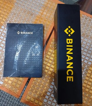 A black Binance-branded notebook and box displayed on a woven bamboo surface.