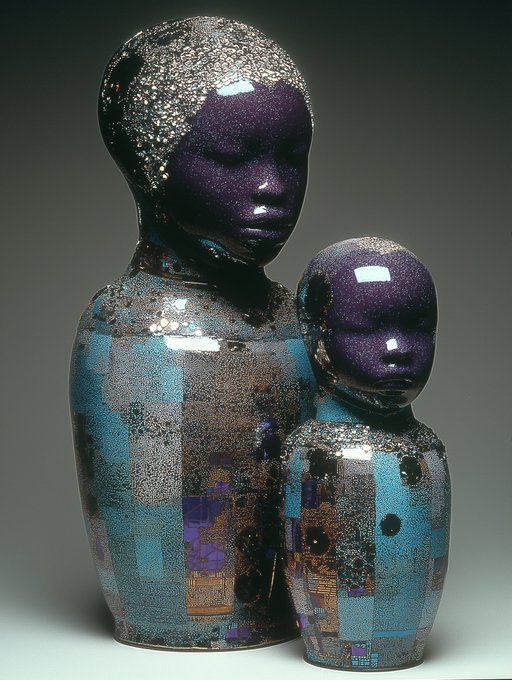 Two glossy ceramic sculptures with purple glazed faces and crackled blue and brown patterned bodies sit against a dark background.