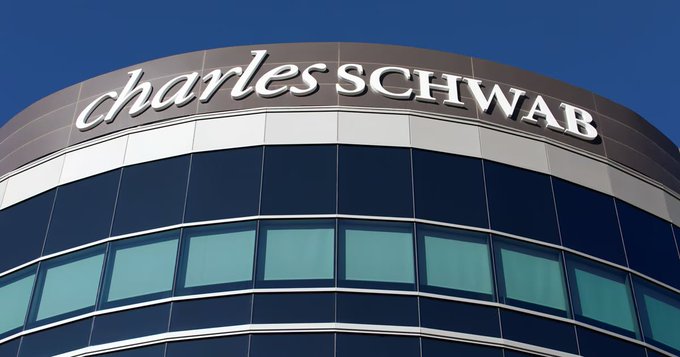 The upper portion of a curved glass office building displays the silver "charles SCHWAB" corporate logo against a clear blue sky.