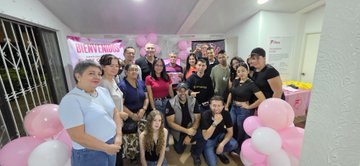 A group of people, including adults and children, pose together indoors at a party decorated with pink and white balloons and a 'Baby Shower' banner.