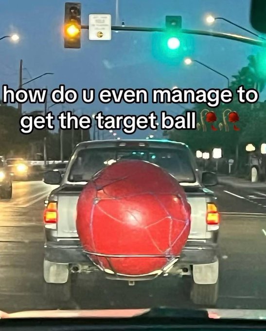 A meme showing a pickup truck on a road with an oversized red Target ball mounted on its rear. Overlaid text reads 'how do u even manage to get the target ball' with two wilted rose emojis.