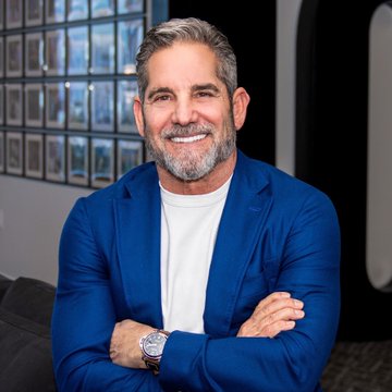 A professional photo of a smiling man with graying hair and a beard, wearing a blue blazer over a white shirt, with his arms crossed and a silver watch visible.