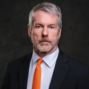 A distinguished-looking man with silver hair and a gray beard, wearing a black suit with an orange tie, poses for a professional portrait against a dark background. The image likely depicts Michael Saylor, the executive chairman of MicroStrategy (now known as "Strategy"), whose company has notably purchased 1,666 BTC valued at $138 million as part of its aggressive Bitcoin acquisition strategy.