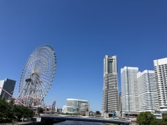 The image features a cityscape with tall buildings, including one that appears to be a skyscraper or a large office building. In the foreground of the photo, there are two ferris wheels - one located closer to the left side of the frame and another further back on the right side. The sky above is blue, indicating clear weather conditions for the day.