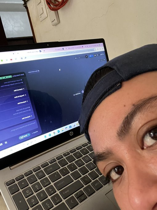 A close-up selfie shows a person wearing a backwards cap, with an HP laptop in the background displaying what appears to be a coding or web development interface.