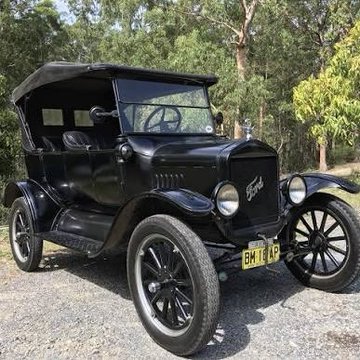 A black vintage Ford Model T car parked on gravel with trees in the background, displaying a yellow license plate reading 'BH 13 47'.