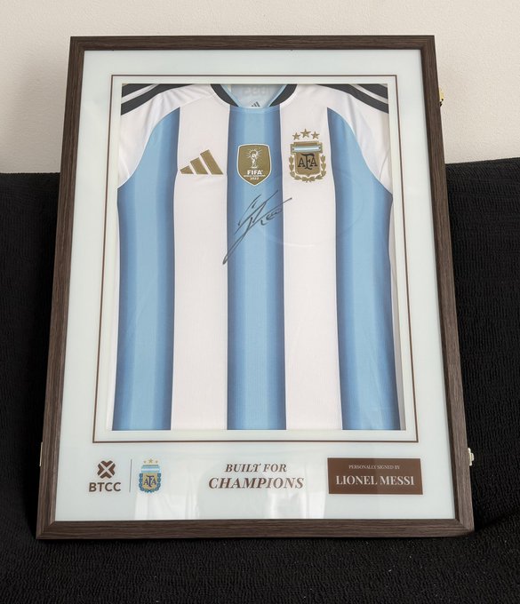 A framed Argentina national team jersey signed by Lionel Messi, featuring the AFA crest, FIFA World Champions badge, and "Built for Champions" text, with a plaque reading "BTCC" and "Personally Signed By Lionel Messi." The image directly supports the post, showing the Messi-signed jersey gifted by the BTCC exchange.