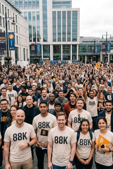 A large group of people wearing matching "88K" Bitcoin-themed t-shirts gather in an urban plaza, with one person holding an orange flag displaying the Bitcoin "₿" symbol and another holding a sign reading "BITCOIN 88K." The image ties to the post "Pek yakında… $BTC" ("Coming very soon… $BTC") by visually promoting a celebratory gathering anticipating Bitcoin reaching the $88,000 milestone.