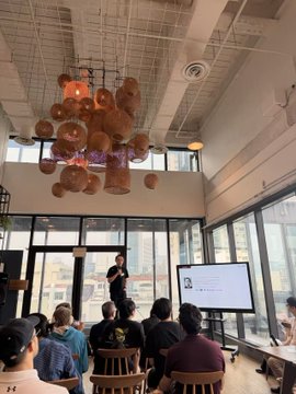 A speaker presents a slide featuring the "Kite" logo to an audience in a bright, modern venue with distinctive copper-colored pendant lights hanging from the ceiling, in connection with the TOKEN2049 Singapore keynote on AI agent identity, authorization, and payments.
