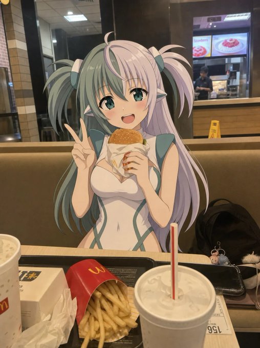 An anime-style character cutout with teal hair and elf ears holds a burger in a McDonald's restaurant, with McDonald's fries, drinks, and a McBag visible on the table in front.