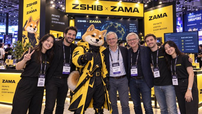 A group photo at the TOKEN2049 Singapore event featuring the ZSHIB x ZAMA booth with their dog mascot, showing team members in branded shirts.