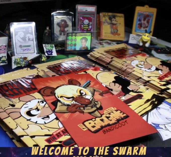 A merchandise table displaying collectibles, posters, and game cards including "The Little Bandicoot," with text reading "WELCOME TO THE SWARM" at the bottom.