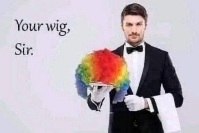 The image features a man dressed in a suit, holding a wig with rainbow colors, possibly for a costume party or event. The caption of the image reads "Your wig, Sir." This suggests that the man might be participating in an event where he is required to wear a unique and colorful wig as part of his attire.