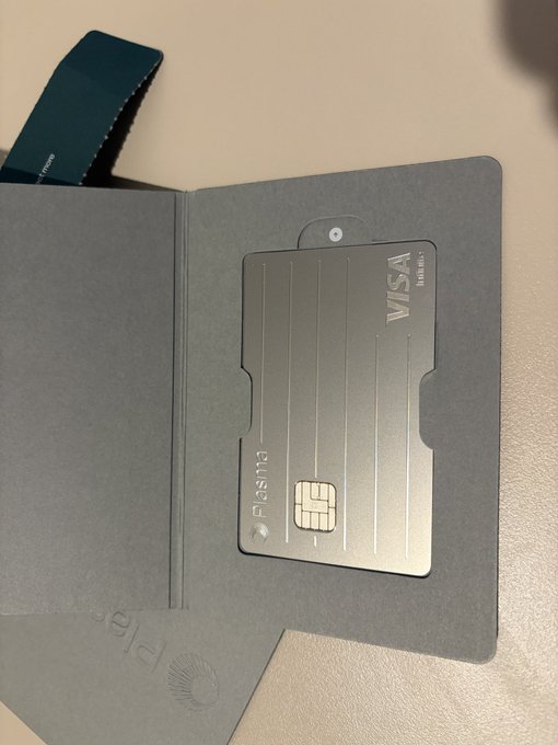 A sleek, metallic Visa Infinite credit card branded "Plasma" is displayed inside a dark gray cardholder, with a teal ribbon accent visible in the background, showcasing the premium unboxing experience described in the post.