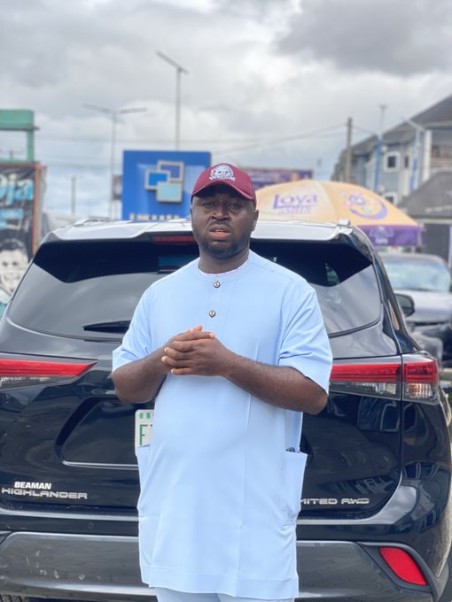 A man in a light blue traditional outfit and red cap stands in front of a black Toyota Highlander Limited 4WD (with a green "E" plate), celebrating his new SUV in Port Harcourt. The post's triumphant tone matches the image, suggesting the vehicle is his recent blessing and the answer to "guess whose car."