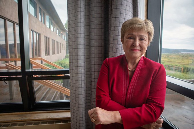 A woman in a red blazer and pearl necklace stands by a window with a scenic view, smiling at the camera; the post suggests she is an IMF representative discussing XRP's role in the new financial system.
