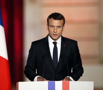 French President Emmanuel Macron stands at a podium, with a French flag visible behind him, as French lawmakers approve a new 31.4% tax on crypto-to-stablecoin swaps set to take effect in 2027.