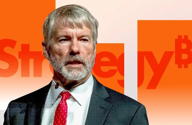 A man with gray hair and beard wearing a suit and red tie speaks in front of an orange backdrop with partial Bitcoin/currency-related text visible.