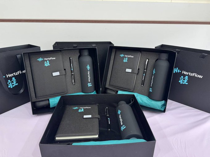 Several branded corporate gift sets from 'HertzFlow' displayed in black boxes, each containing a notebook, water bottle, and pen.