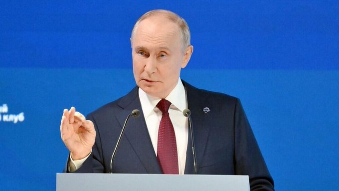A man in a dark suit and red tie speaks at a podium against a blue backdrop, gesturing with his hand as he addresses an audience. The image accompanies news coverage of Russian President Vladimir Putin's remarks on AI governance, where he emphasized that AI should remain a tool controlled by humans and that final decisions must be made by people.