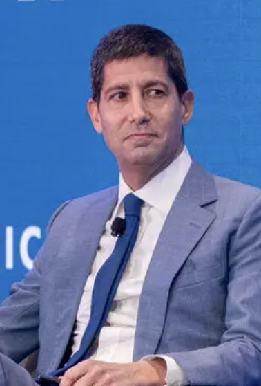 A man in a gray suit and blue tie is seated against a blue backdrop with partial white text visible, likely appearing at a financial conference or panel discussion. The image relates to the post about weakening Fed rate hike expectations following unexpectedly poor U.S. payrolls data, suggesting he may be a financial expert or analyst commenting on the labor market's surprising decline.