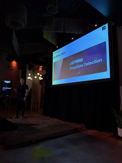 A presenter stands on a small stage next to a large projection screen displaying a slide titled 'xBITMIND Deepfake Detection' under a 'PROJECT BITMIND SNG24' header.