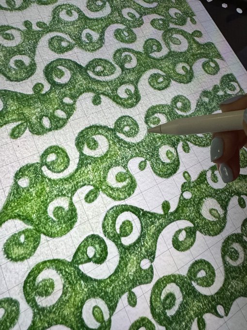 A hand with a pen points to a detailed green ink drawing featuring intricate swirling wave patterns on grid paper, showcasing the artwork being shared in celebration of its first edition NFT collection. The hand-drawn piece reflects the organic, flowing green design that the artist is excited to have acquired by @nft_clctr.