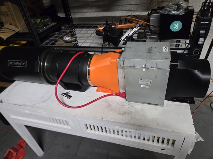 An industrial AC Infinity fan setup with an orange connector and red hose sits on a white cabinet next to a metal enclosure.
