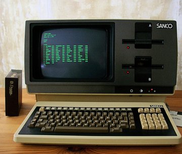 llorco A-sanco computer monitor displays green text, accompanied by a black keyboard and mouse on a wooden desk.