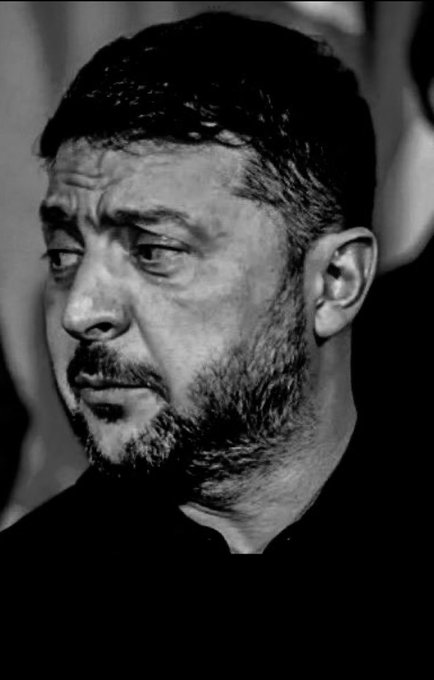 A black and white close-up portrait of a bearded man with dark hair looking off to the side with a serious expression.
