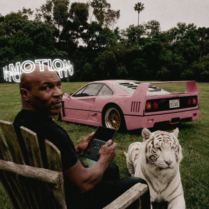 A surreal image showing Mike Tyson sitting in a wooden chair holding a Nintendo Game Boy, with a white tiger beside him and a pink Ferrari F40 in the background with an 'IN MOTION' neon sign.