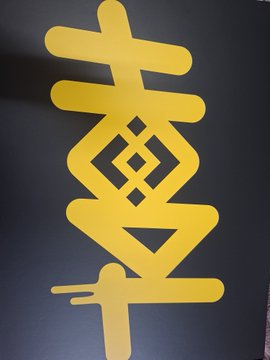 A yellow cutout design of the Binance logo, featuring the company's distinctive geometric "B" symbol, is displayed against a black background, likely included as promotional material within the Binance 9-Year Anniversary HODL Gift Box.