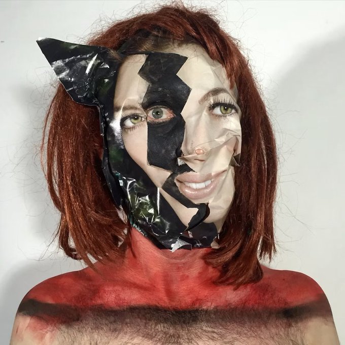 An artistic portrait of a red-haired woman with a fragmented face, where parts of her skin appear to be peeling away as if made of tape or plastic, revealing green eyes beneath.