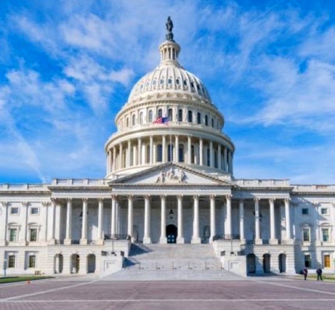 The United States Capitol building in Washington, D.C., with its iconic dome and American flag, under a blue sky with wispy clouds.