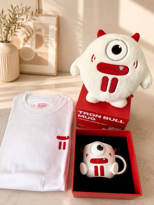 Product photo displaying a 'TRON BULL' ceramic coffee mug merchandise set, including a red plush toy and a folded white t-shirt in a brightly lit room.