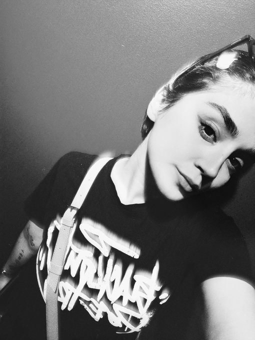 A black-and-white selfie of a young woman with sunglasses perched on her head, wearing a graphic t-shirt, gazes directly at the camera with a subtle expression that matches the casual, self-introductory tone of her post "Hello it's Sariraa."