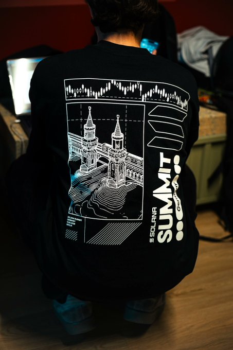 A back view of a person wearing a black Solanqr Summit t-shirt featuring a white line-art design of a cathedral/temple with "SOLANQR SUMMIT" text printed on it.