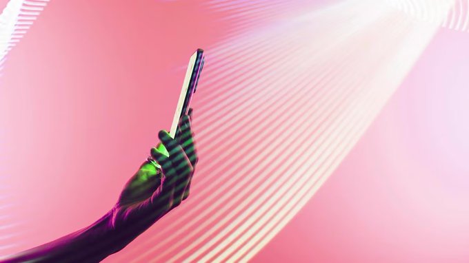 An artistic photo of a hand holding up a glowing green bottle against a vibrant pink and white wavy background.