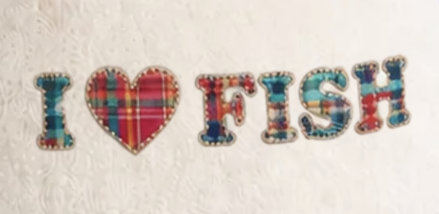 Decorative fabric letters spelling 'I ❤ IRISH' with patchwork patterns, resting on a white lace surface.