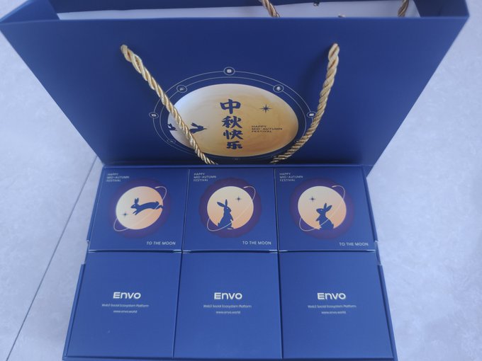 A blue gift bag and matching boxes from 'Envo' featuring 'Mid-Autumn Festival' greetings, a moon design with a rabbit silhouette, and the text 'TO THE MOON' along with Chinese characters.