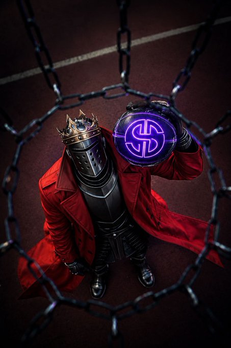 A figure wearing a red coat, metal armor, and a crown stands behind chains, holding a glowing purple orb with a dollar sign symbol.
