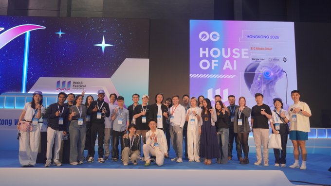 A large group of participants poses together on stage at the "House of AI" event in Hong Kong 2026, hosted in partnership with the Web3 Festival and 0G, with a robotic dog featured on the screen behind them. The image ties to the post's theme by showcasing the 168 winning teams whose AI agent projects successfully launched on the 0G mainnet, highlighting the real-world production readiness of the platform.