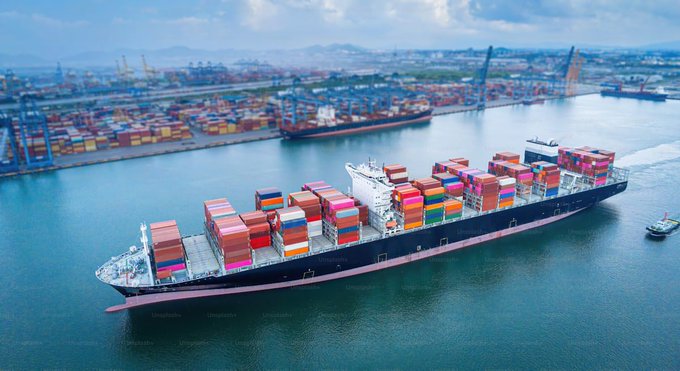 An aerial view of a massive container ship loaded with multicolored shipping containers navigating through a busy port.