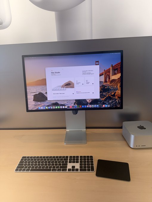 A Mac Studio setup featuring a Studio Display with "Mac Studio" visible on the screen, alongside a Magic Keyboard and trackpad. The image humorously illustrates the joke's premise of installing Tailscale on Apple's devices by showcasing an actual Mac Studio configuration.