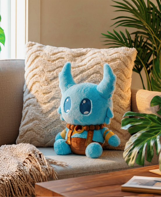 The image features a blue stuffed animal sitting on top of a couch cushion. The plushie appears to be a character from a video game or movie franchise, possibly a dragon or a similar creature. It has a brown band around its neck and is positioned in front of a potted plant, which adds a touch of greenery to the scene. The image also contains some text that reads "Some Key info for the Plushie Drop at 12 pm ET: There will be a separate Koda Plushies site launching for this drop. On that site, you’ll be able to log in with your Glyph wallet". This suggests that there is an upcoming release of the Plushie Drop and users can expect to receive Early Access for their favorite characters from the game or movie franchise.