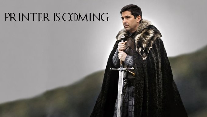 A man dressed in a fur-lined cloak holds a sword upright against a foggy landscape, beneath the text "PRINTER IS COMING" styled after the Game of Thrones logo, parodying the show's iconic opening to announce the imminent arrival of a printer.