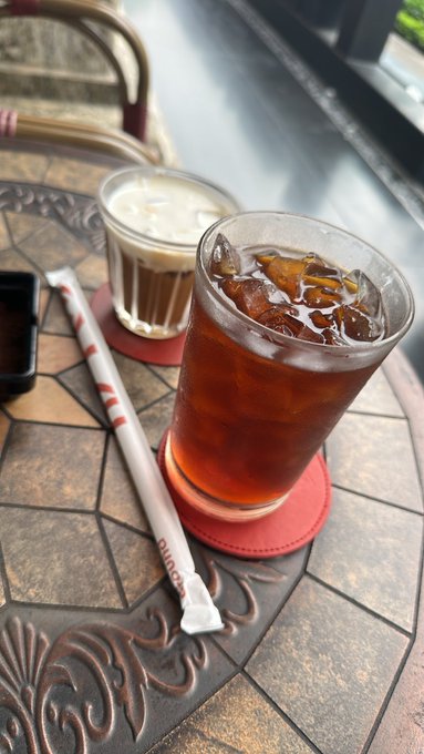 Two iced drinks, one with coffee and one lighter colored, sit on a decorative metal table alongside a paper-wrapped straw.