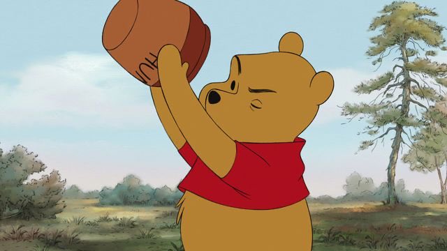 Animated Winnie the Pooh wearing a red shirt holds a large honey pot above his head with a strained expression in an outdoor setting.